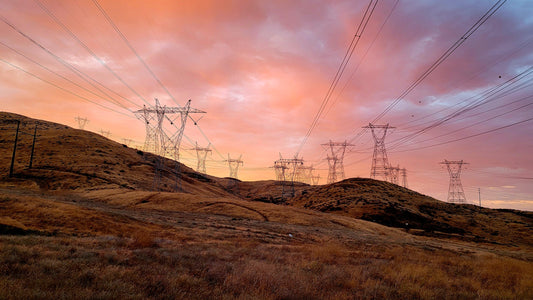 Power lines and transmission towers against a pink and orange sunset sky.