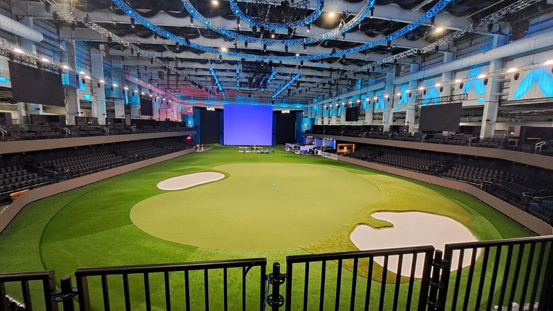 Large indoor sports facility with a green field and seating area.