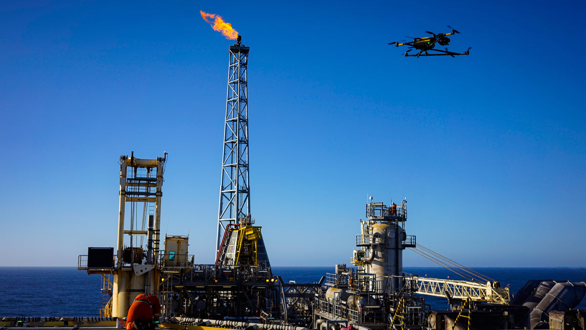 Offshore oil platform with a drone flying above it against a clear blue sky.