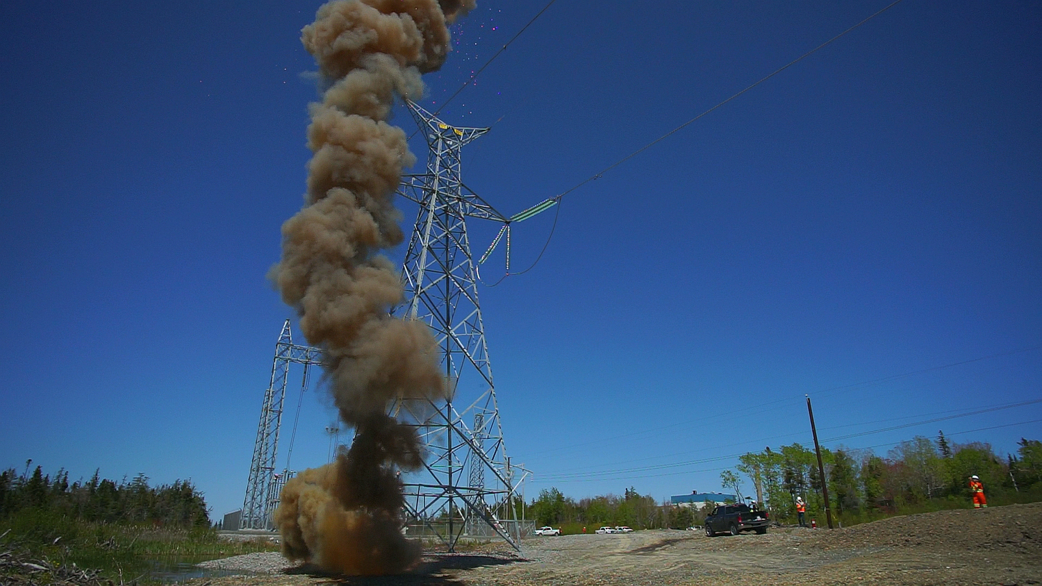 Power line tower with smoke and debris, surrounded by a clear blue sky.
